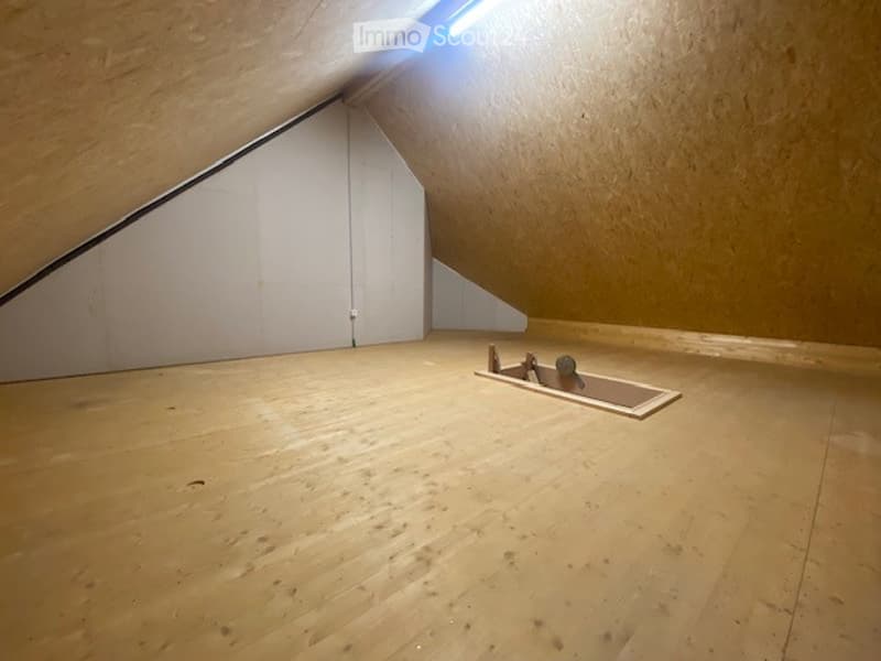 Empty attic space with wooden flooring, slanted wooden ceiling, white walls, and a small built-in platform with a single chair.