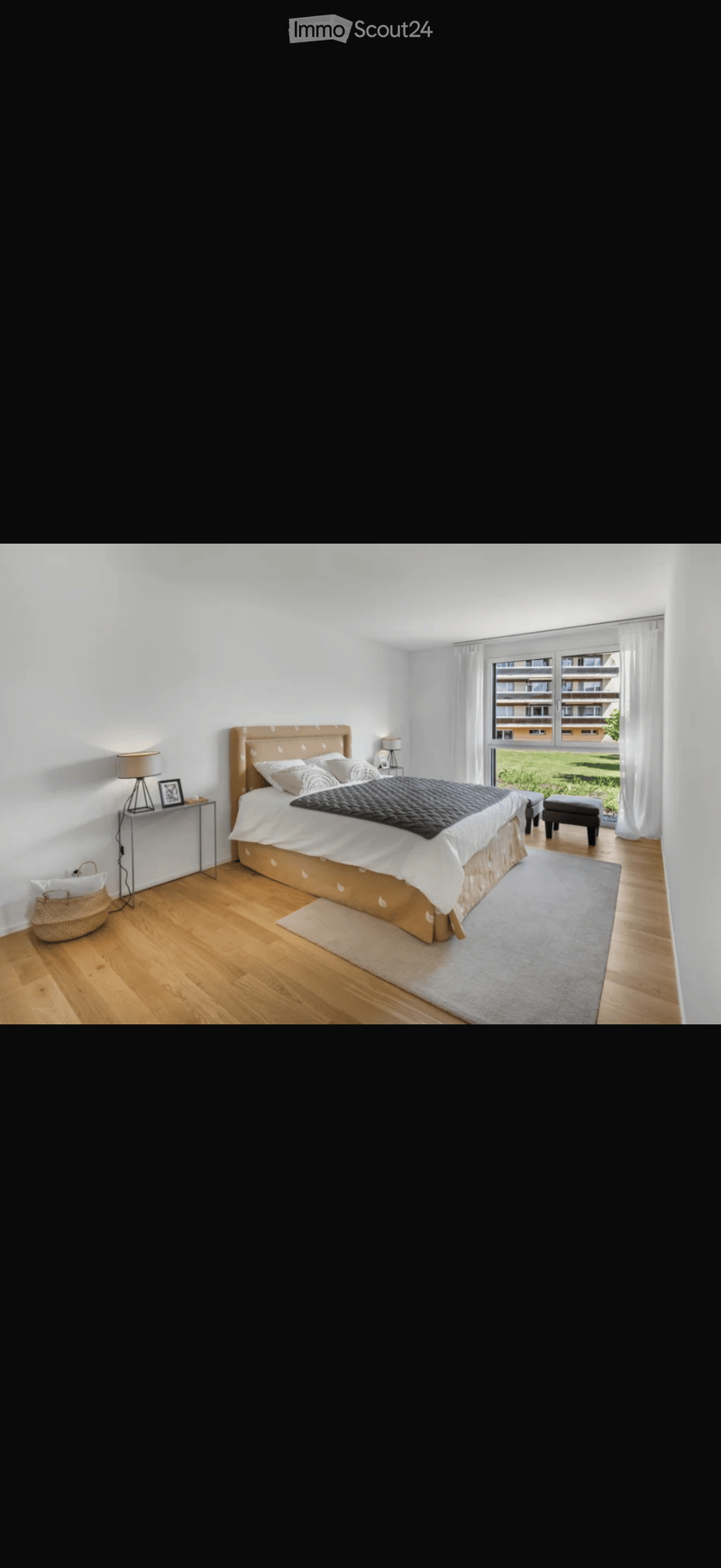 Modern bedroom with a large bed, nightstand, lamp, and a view of a green area through large windows.