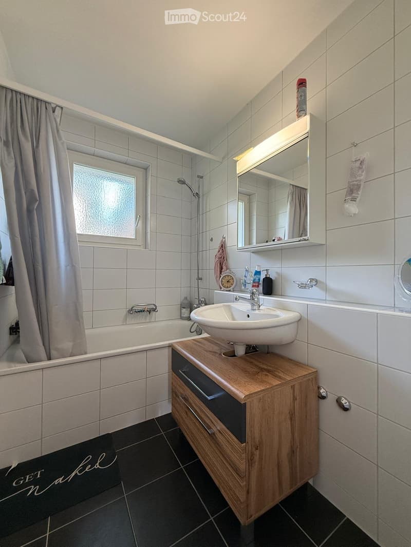 Modern bathroom with a bathtub, sink, mirror, wooden cabinet, and various bathroom accessories.