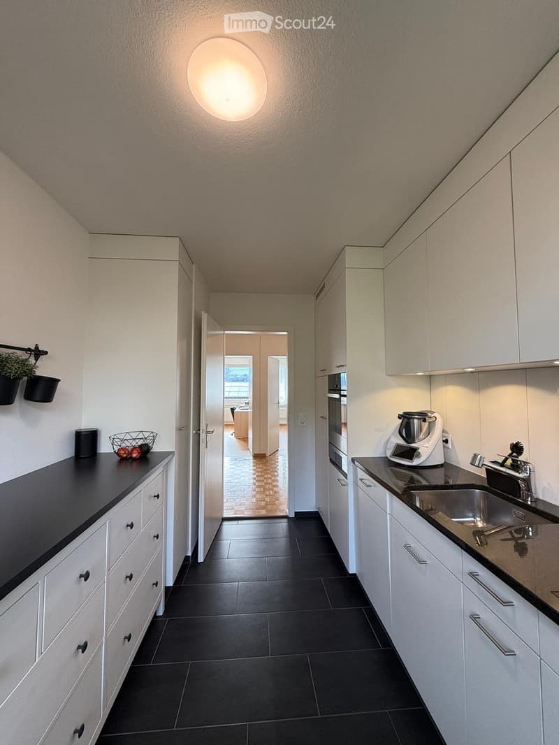 Modern kitchen with white cabinets, black countertops, and stainless steel appliances. Features a sink, oven, and blender on the counter.