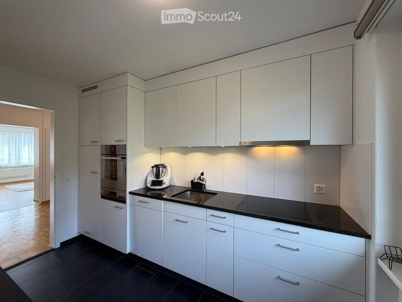 Modern kitchen with white cabinets, black countertops, and stainless steel appliances. Features a sink, faucet, oven, and a blender on the counter.