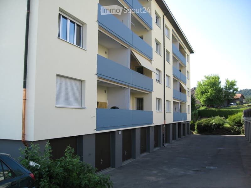 Multi-story residential building with multiple balconies, windows, and a parking area.