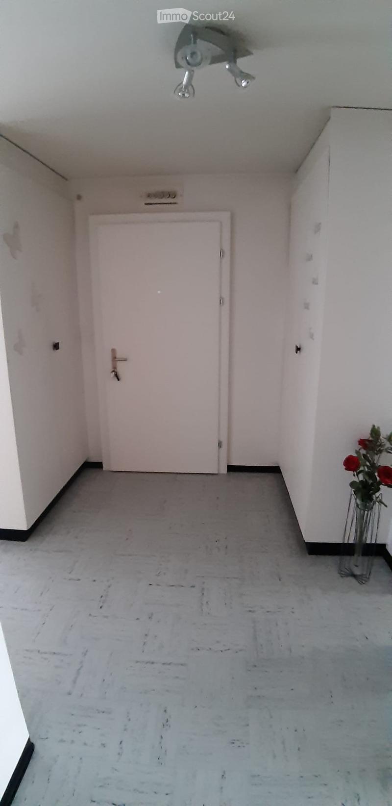 Empty hallway with light-colored walls, a closed door, and a small vase with red flowers on the right side.