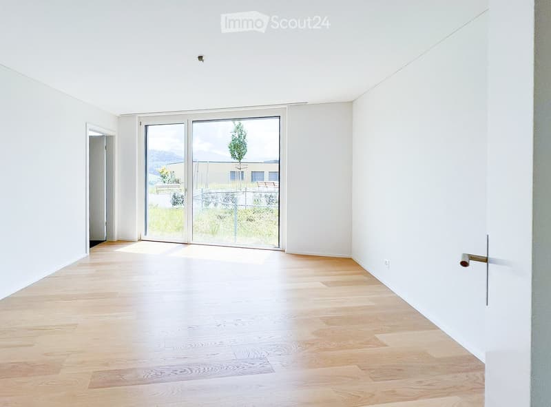 Empty room with light wooden flooring and white walls, featuring a large sliding glass door leading to an outdoor area.