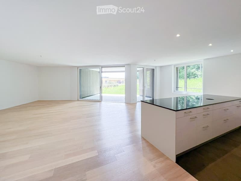 Modern kitchen with light wooden flooring, white cabinets, and a central island with a black countertop.