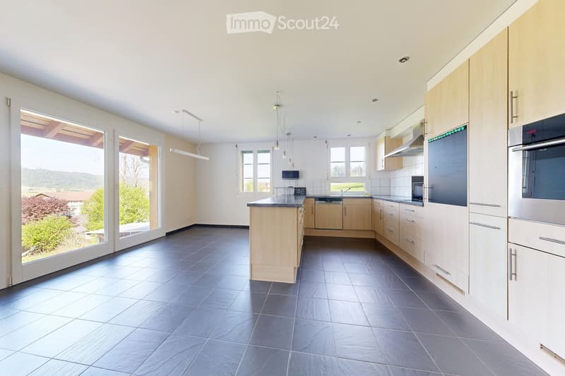 Modern kitchen with light wood cabinets, dark tiled floor, stainless steel appliances, and large windows offering a scenic view.