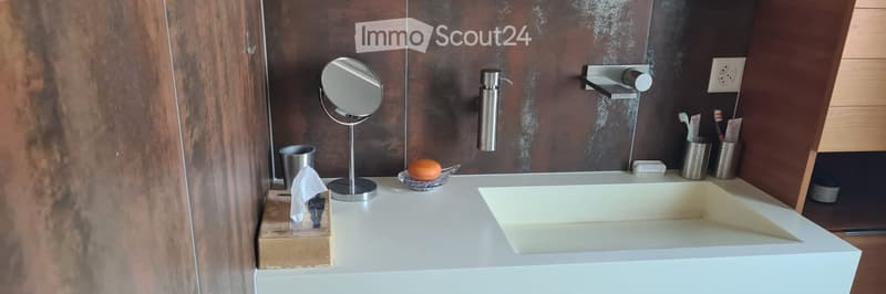 Modern bathroom with a white sink, a round mirror on a stand, a soap dispenser, toothbrush holders, and a tissue box on the counter.