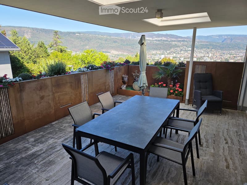 Balcony with a view of the city and mountains, featuring a dining table, chairs, and an umbrella.