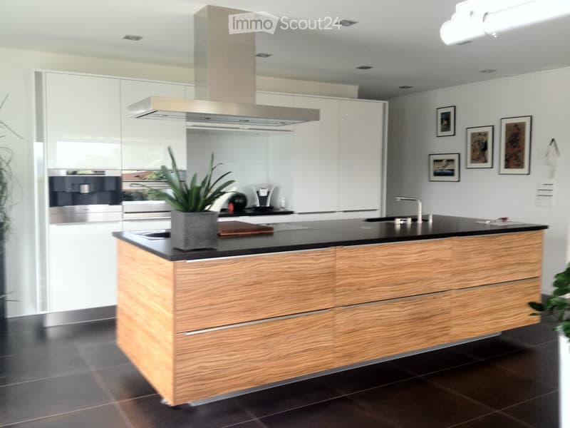 Modern kitchen with a wooden island, black countertop, stainless steel appliances, and framed pictures on the wall.