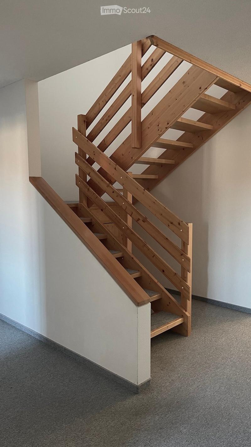 Wooden staircase with open wooden railings and carpeted steps, leading upwards in a modern interior setting.