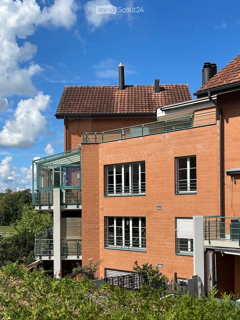 Two-story house with red brick exterior, multiple windows with green railings, and a balcony on the upper level.
