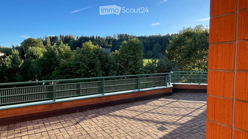 Balcony with brick flooring, green metal railing, and a view of a forested area.