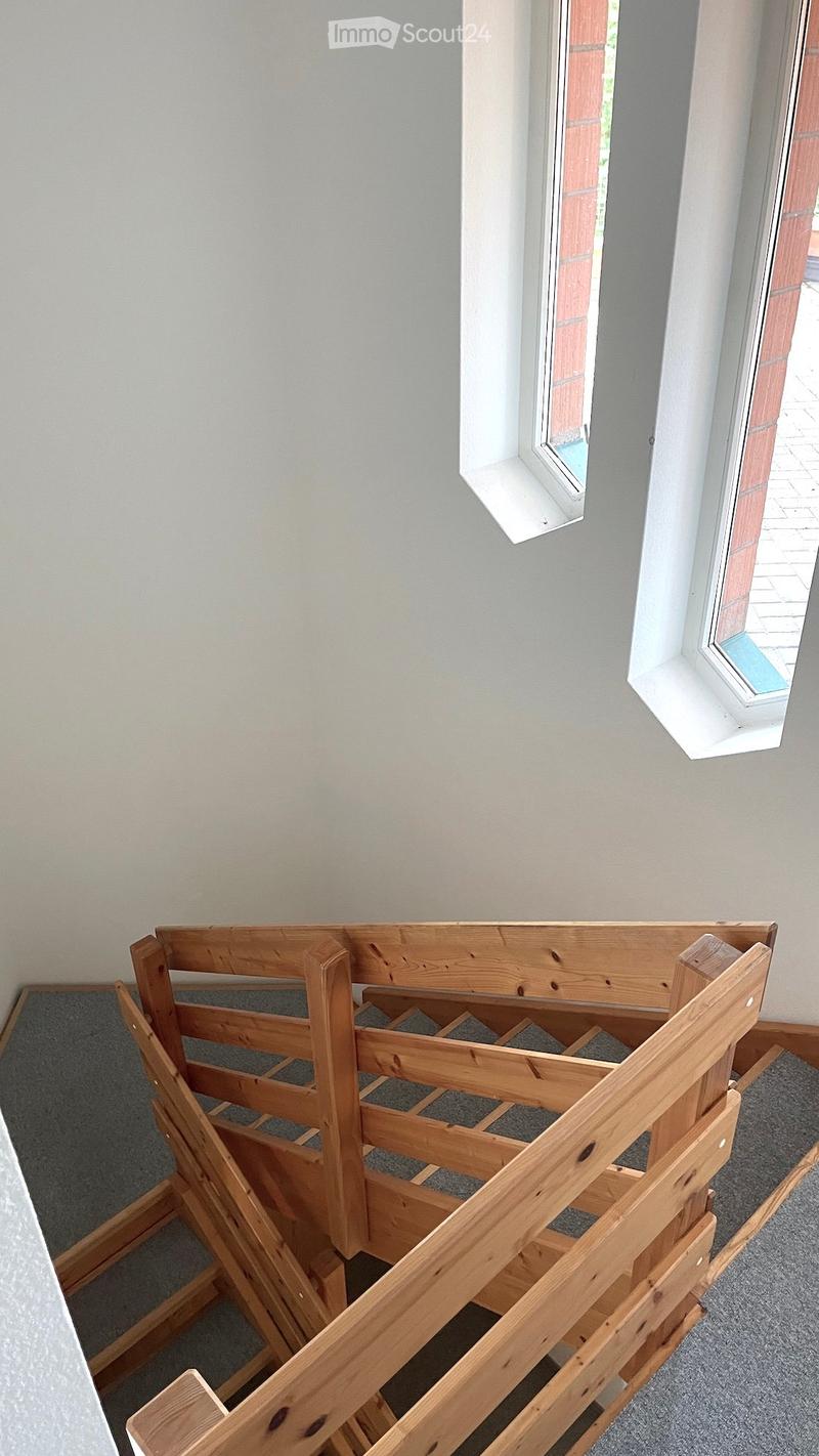 An empty hallway with grey carpeted floor, light grey walls, and two windows with white frames and wooden sills.