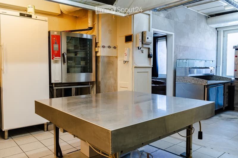 Commercial kitchen with stainless steel surfaces, refrigerator, oven, and counter.