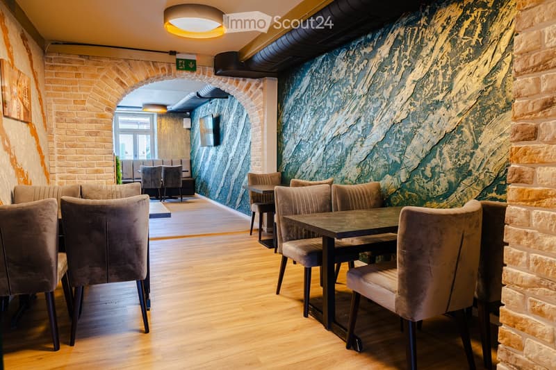 Modern restaurant interior with wooden flooring, brick walls, and a mix of seating including tables, chairs, and a sofa.