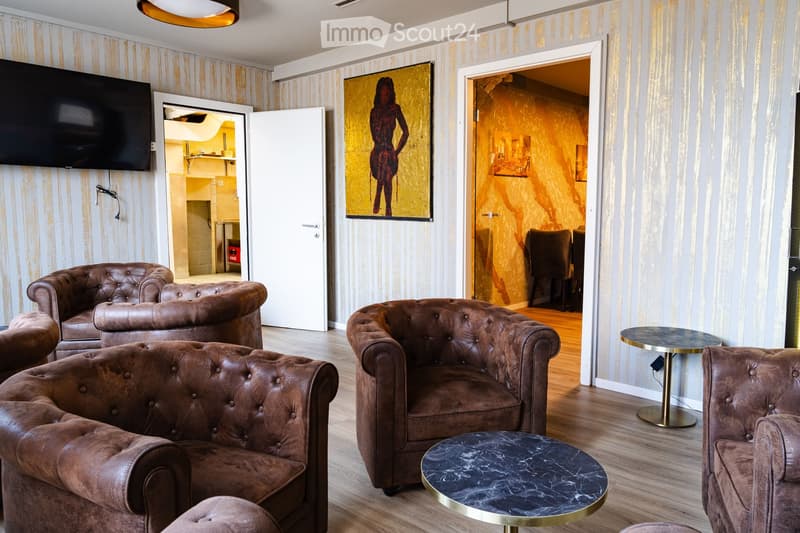 Modern living room with leather sofas, chairs, a coffee table, and a television mounted on the wall. The room features striped wallpaper and a warm, inviting ambiance.