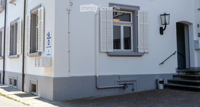 Two-story building with white walls, grey shutters, and a sign indicating parking and hotel information.