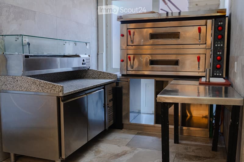 Commercial kitchen with stainless steel ovens, refrigerator, granite countertop, and a metal table.