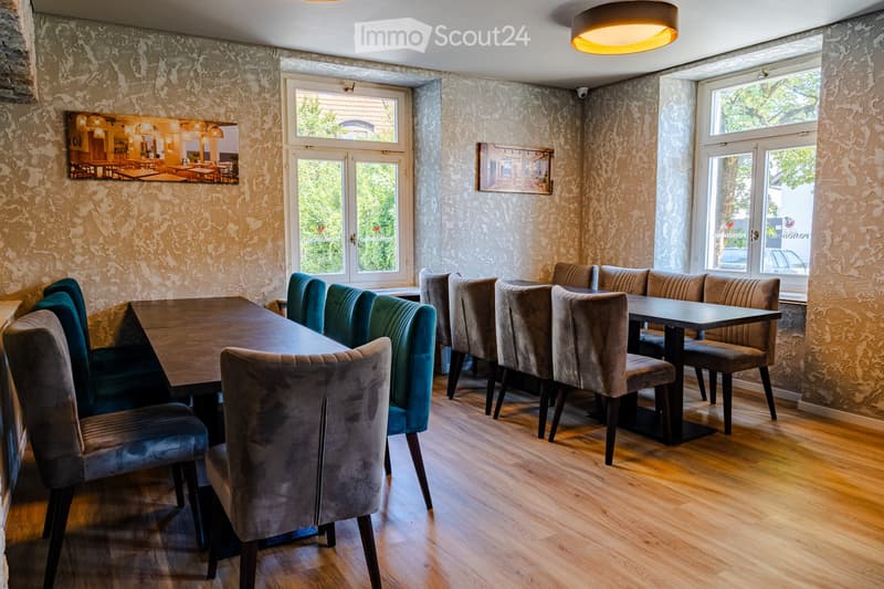 Dining area with wooden floor, large windows, dining table with chairs, picture frames on walls, and modern lighting fixture.