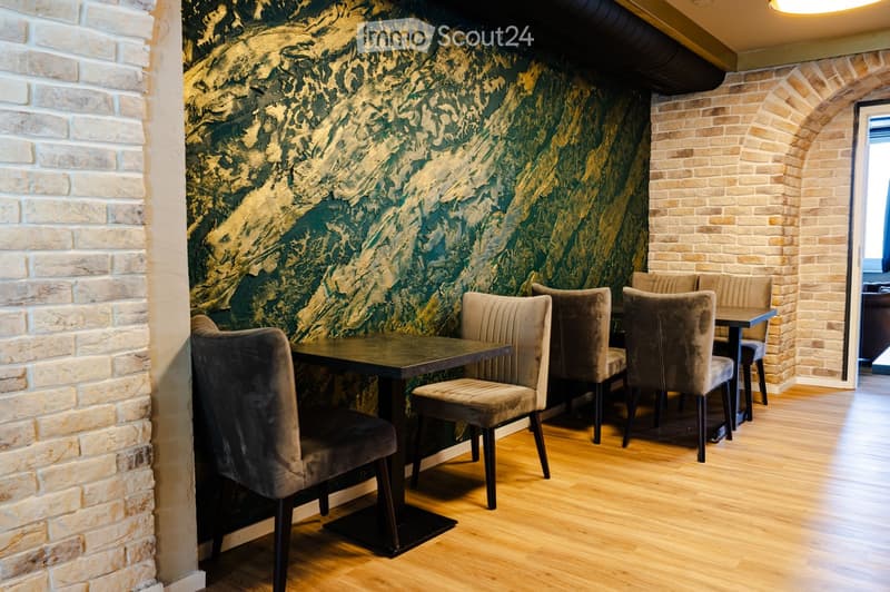 A cozy dining area with a dark wooden table and plush, upholstered chairs, set against a textured green and gold wall with exposed brick accents.