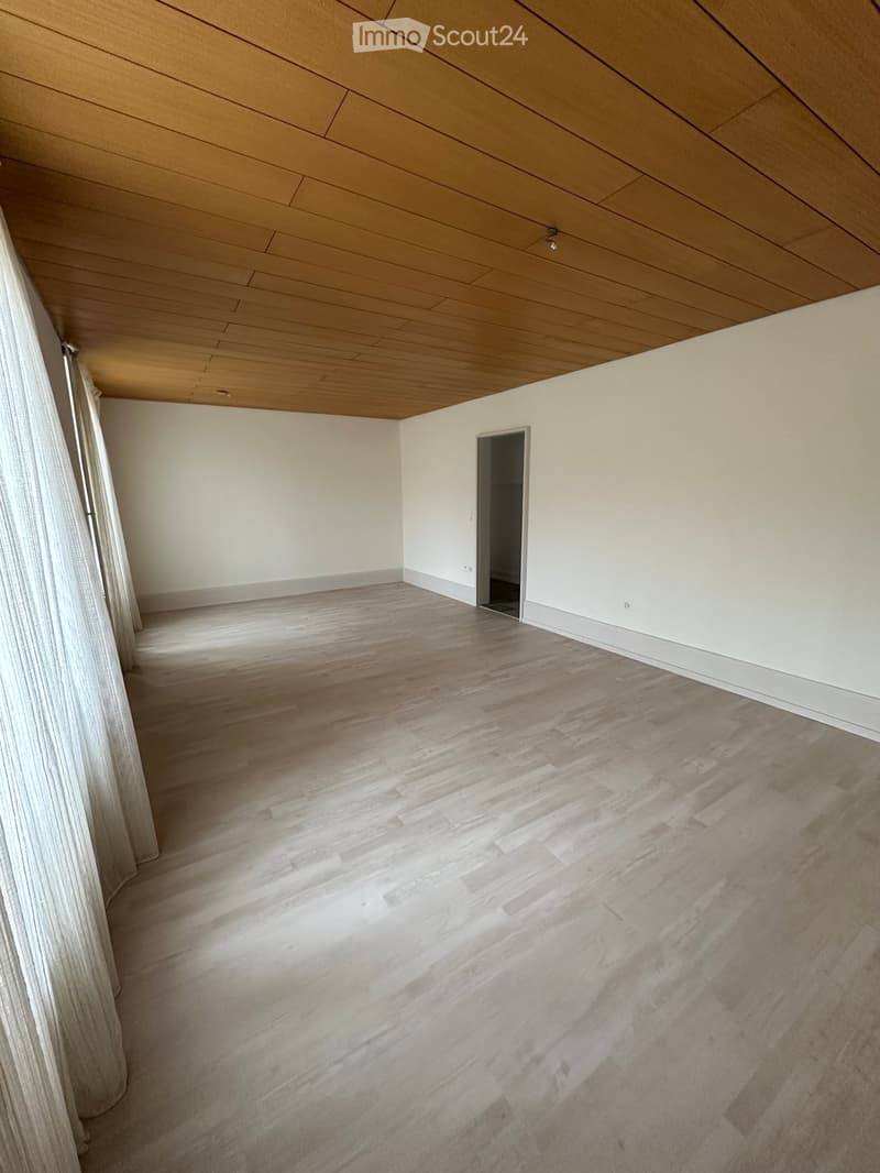 Unfurnished Room. An empty room with white walls, wooden ceiling, and wooden flooring. There are two white curtains on the left side and a door on the right side.