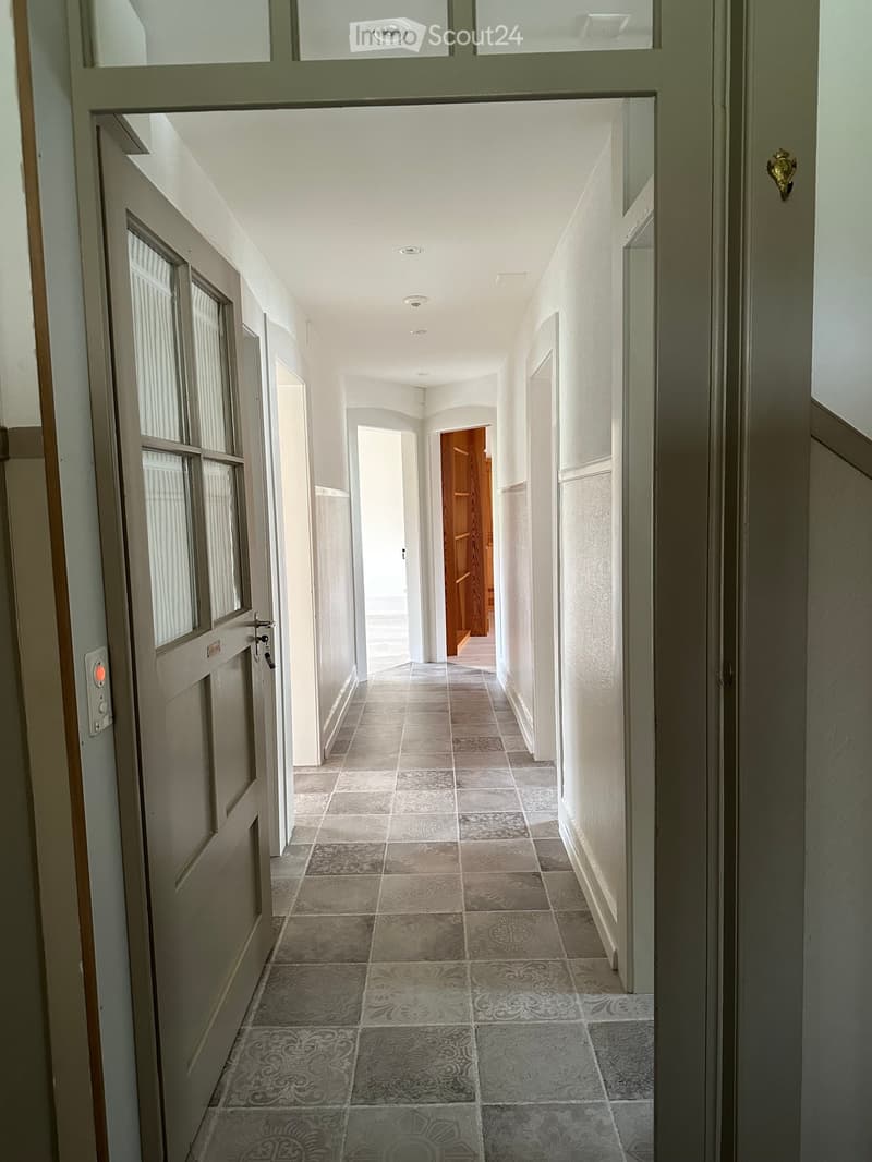 Corridor / Hallway. Empty hallway with tiled floor, white walls, and doors on both sides.