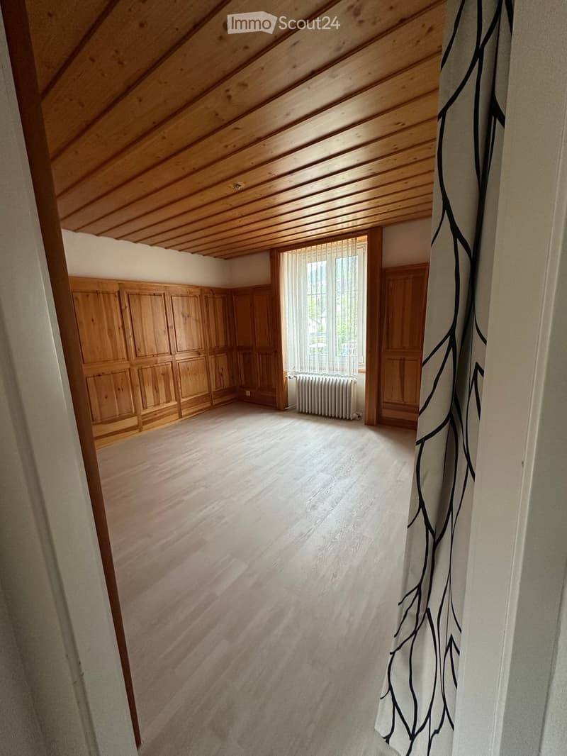Unfurnished Room. Empty room with wooden paneling on the walls, wooden ceiling, and white floor. There is a window with white curtains and a white radiator below it.