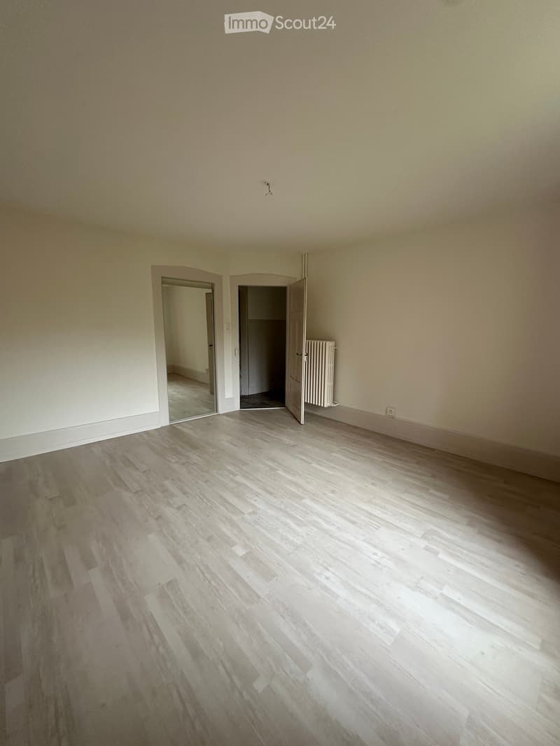 Unfurnished Room. Empty room with white walls, wooden floor, and two doors leading to other rooms. A radiator is mounted on the wall.