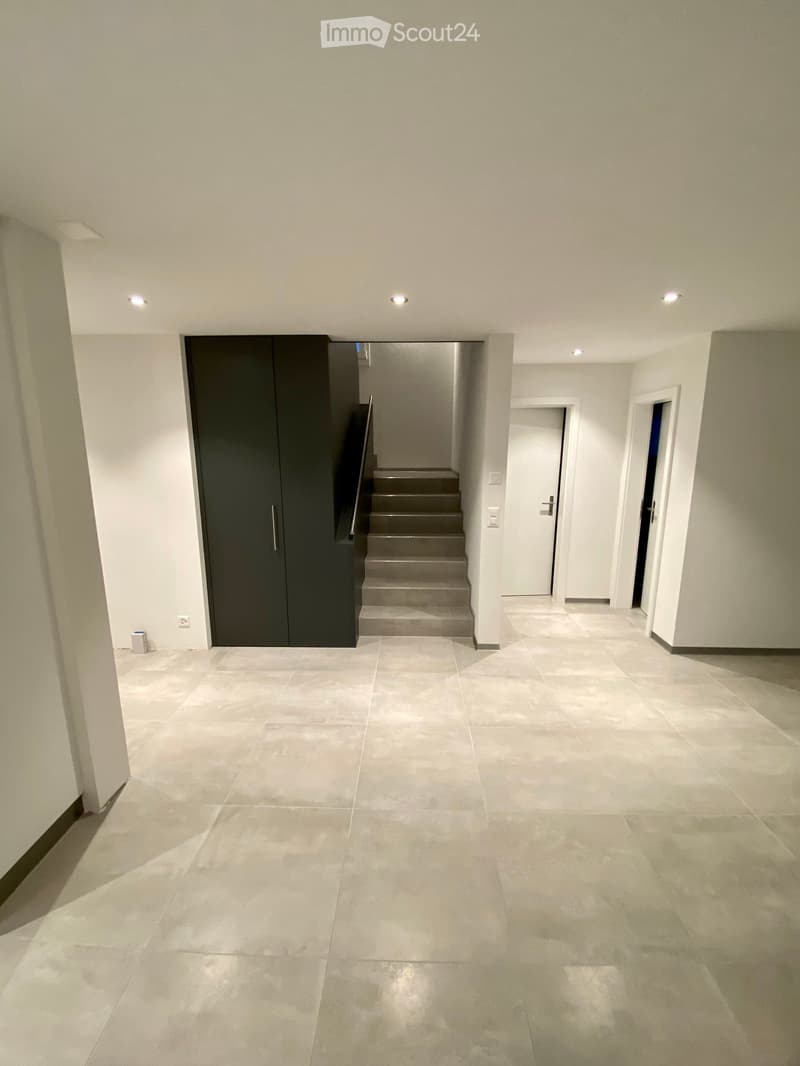Empty hallway with tiled floor, white walls, recessed lighting, and a staircase leading upwards.