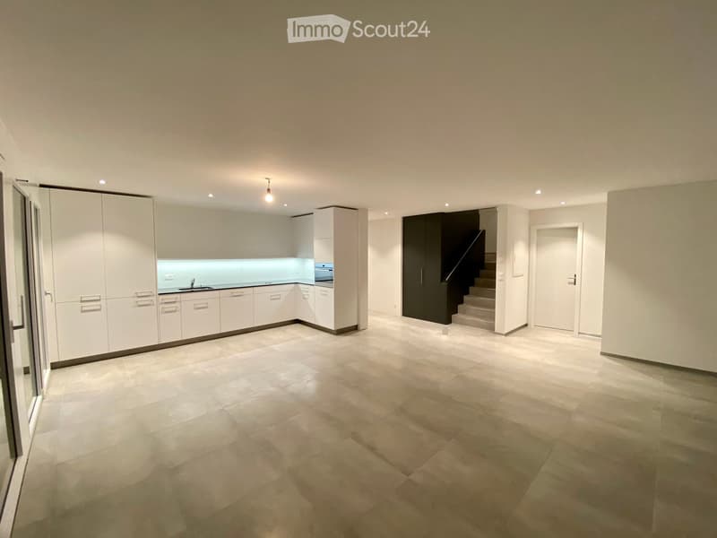 Modern kitchen with white cabinets, a sink, and a stove, featuring a light blue backsplash and a spacious open layout with a staircase leading to another level.