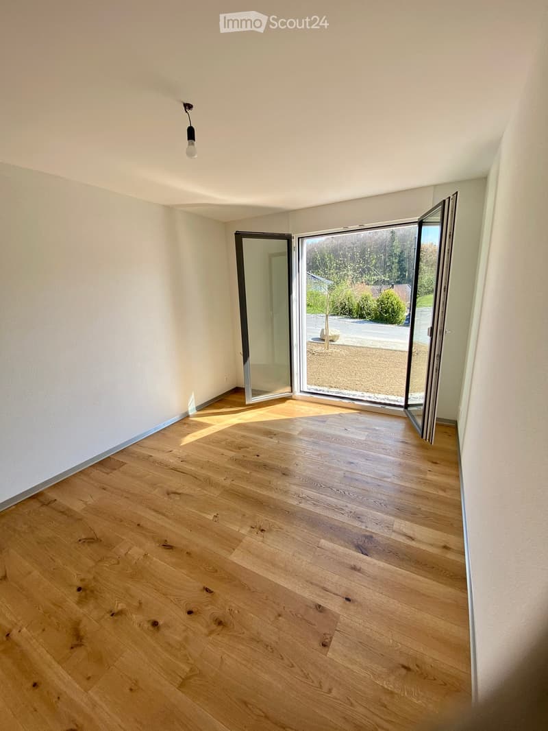 Empty room with light wooden flooring, white walls, and large sliding glass doors leading to an outdoor area.