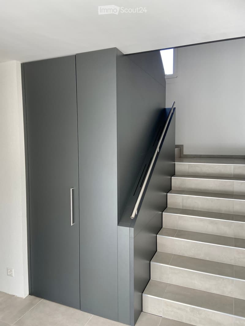 Modern staircase with grey steps and a sleek metal railing, adjacent to a grey wall with a door.