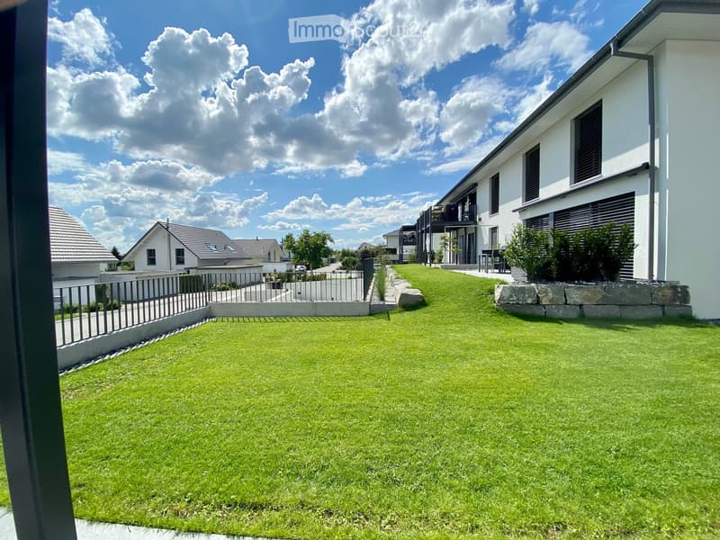 Well-maintained lawn with a modern house in the background, featuring a balcony and surrounding greenery.