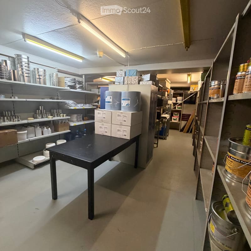 Storage area with shelves holding cans, pails, and boxes, a black table in the center, and additional storage units in the background.