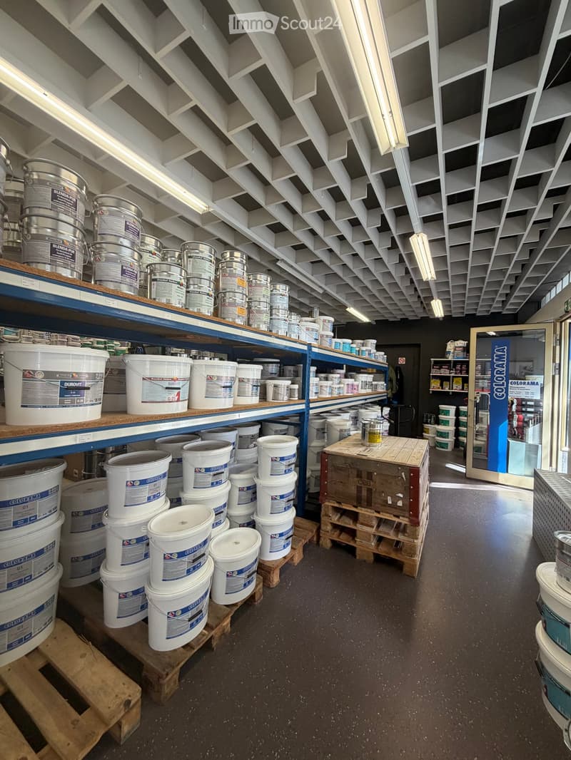 A store aisle with shelves stocked with various paint buckets and containers, organized on wooden pallets and shelves.