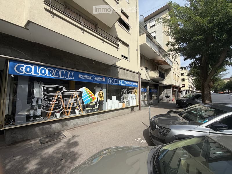Multi-story building with storefront labeled "COLORAMA" displaying paint products and mannequins, with parked cars in front.