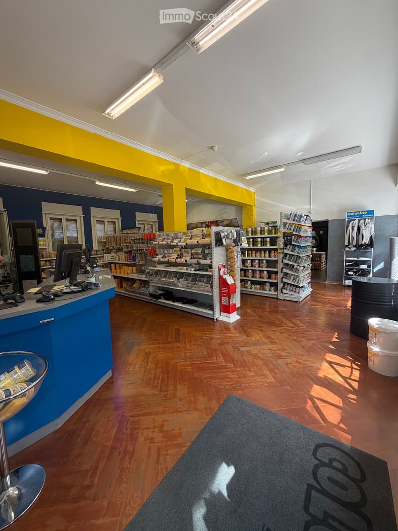 Retail store interior with wooden flooring, blue and yellow walls, shelves stocked with products, a counter with a computer, and clothing racks.