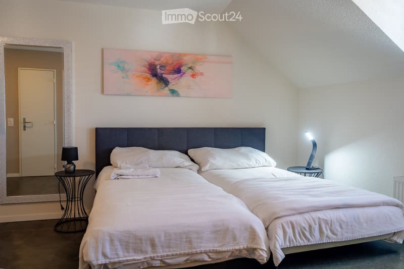 Cozy bedroom with a double bed, nightstands, lamps, a large mirror, and a colorful abstract painting on the wall.