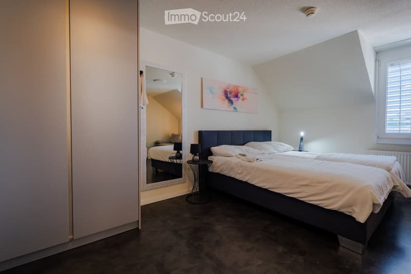 Cozy bedroom with two single beds, nightstands, lamps, a large mirror, and a colorful painting on the wall.