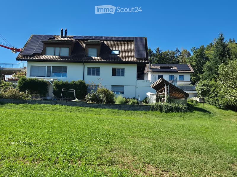 Two-story house with solar panels on the roof, surrounded by a well-maintained lawn and trees.