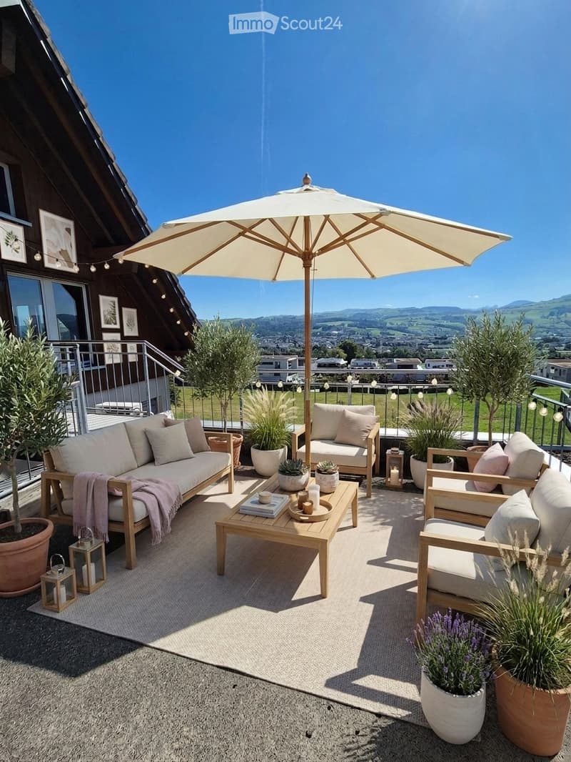 A modern outdoor terrace with a sofa, coffee table, chairs, umbrella, and potted plants, overlooking a scenic valley view.