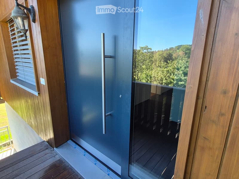 Balcony with wooden decking, glass sliding door, and outdoor lighting fixture on the wall.