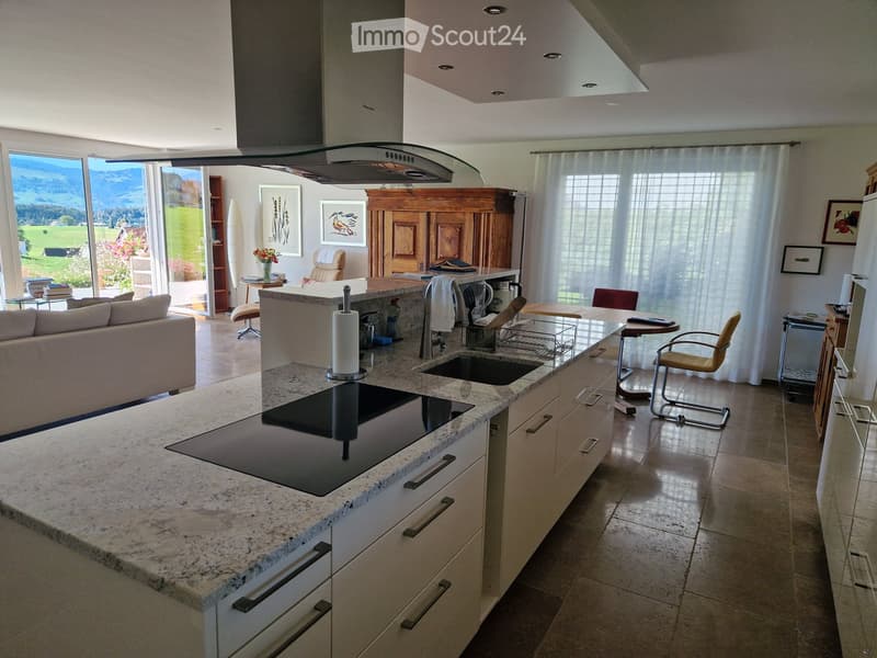 Open-plan kitchen and living area with a large island, granite countertops, modern appliances, and large windows offering a scenic view.
