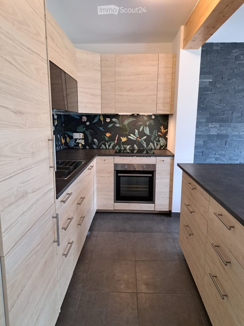 Modern kitchen with light wooden cabinets, stainless steel oven, and dark countertops.