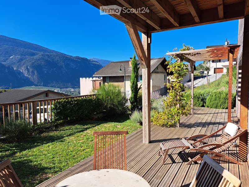Wooden deck with lounge chairs, table, and a view of mountains and surrounding houses.