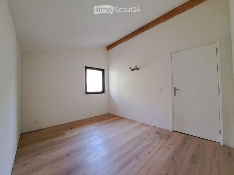 Empty room with wooden flooring, white walls, a single window, and a closed white door.