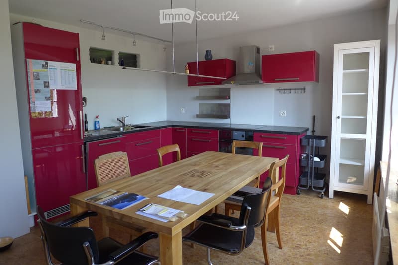 Modern kitchen with red cabinets, a wooden dining table, and various appliances including a refrigerator, sink, oven, and dishwasher.