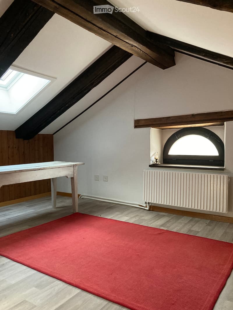 An attic room with wooden beams, skylights, a small table, a radiator, and a mounted screen.