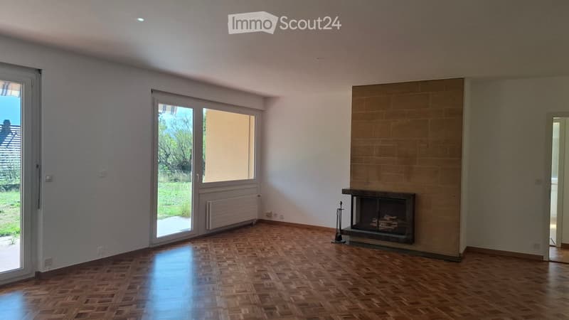 Empty room with wooden parquet flooring, white walls, large windows, and a fireplace with a tiled surround.