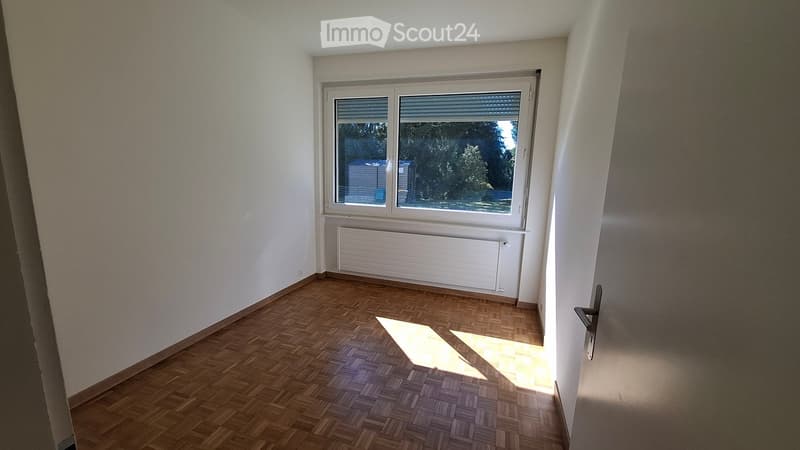 Empty room with wooden flooring, white walls, a window with blinds, and a radiator below the window. No furniture or personal items are present.